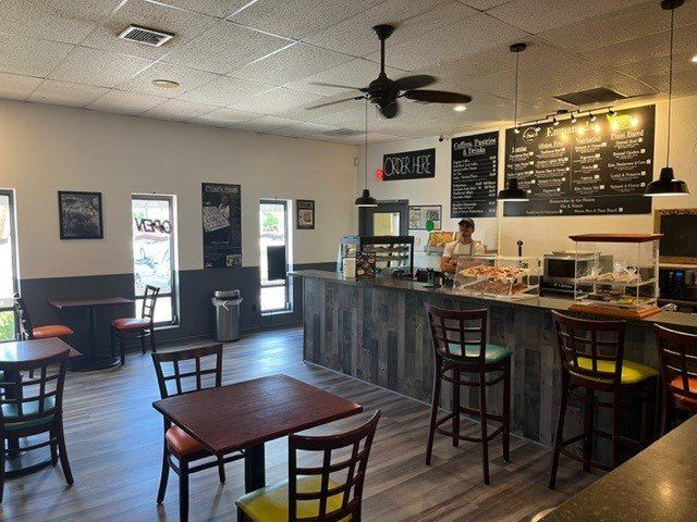 Interior of a cafe: tables with colorful chairs, counter with pastries, menu board, and barista.