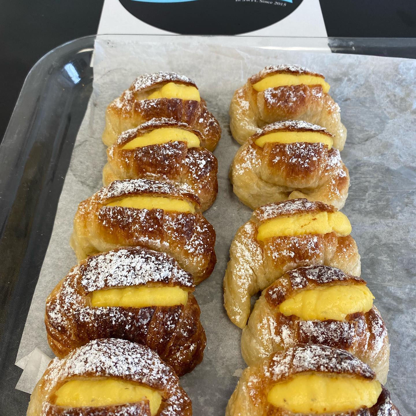 Pastries with custard filling dusted with powdered sugar on a tray.