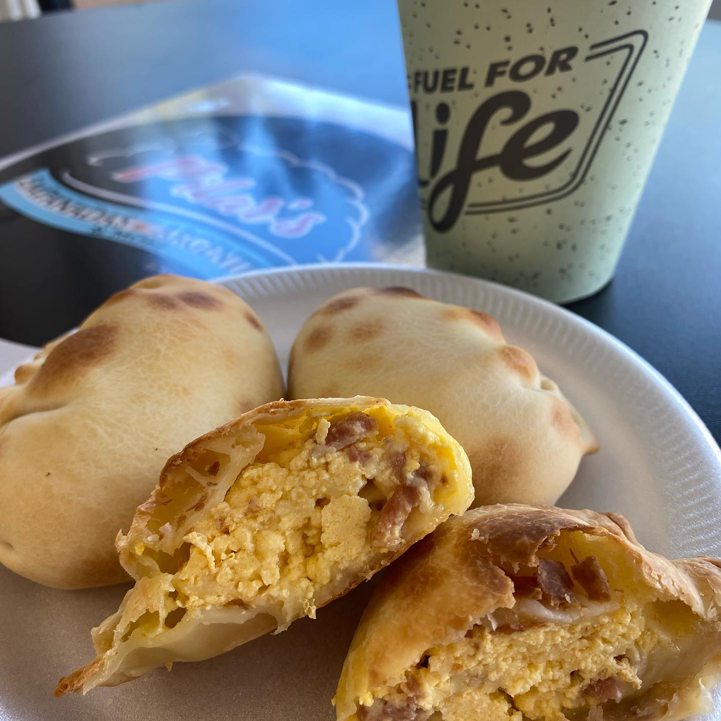 Empanadas on a plate with a drink and a logo in the background. One empanada is cut open, showing the filling.