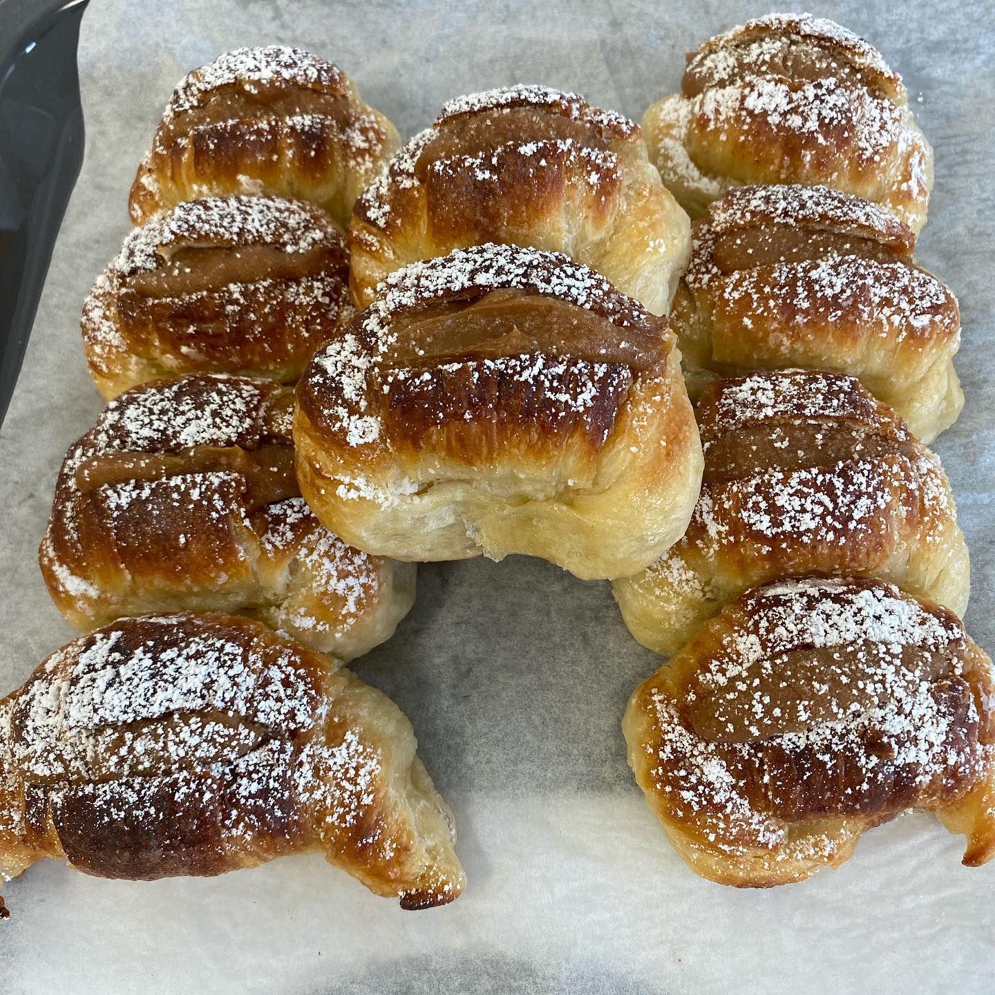 Golden, glazed pastries sprinkled with powdered sugar arranged on parchment paper.