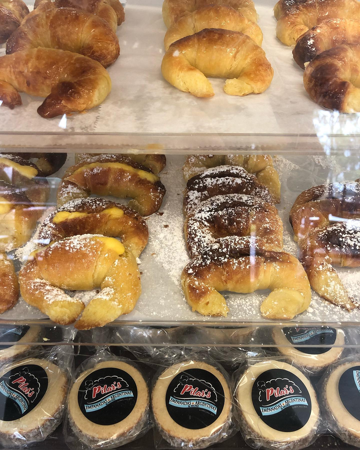 Pastries in a bakery display case, including croissants and cookies, dusted with powdered sugar.