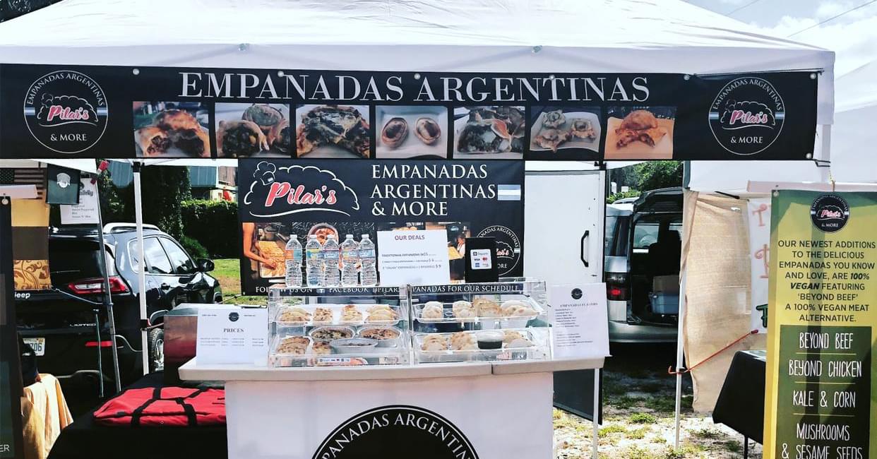 Empanadas Argentinas food stall at an outdoor market, displaying empanadas, with a banner and menu.