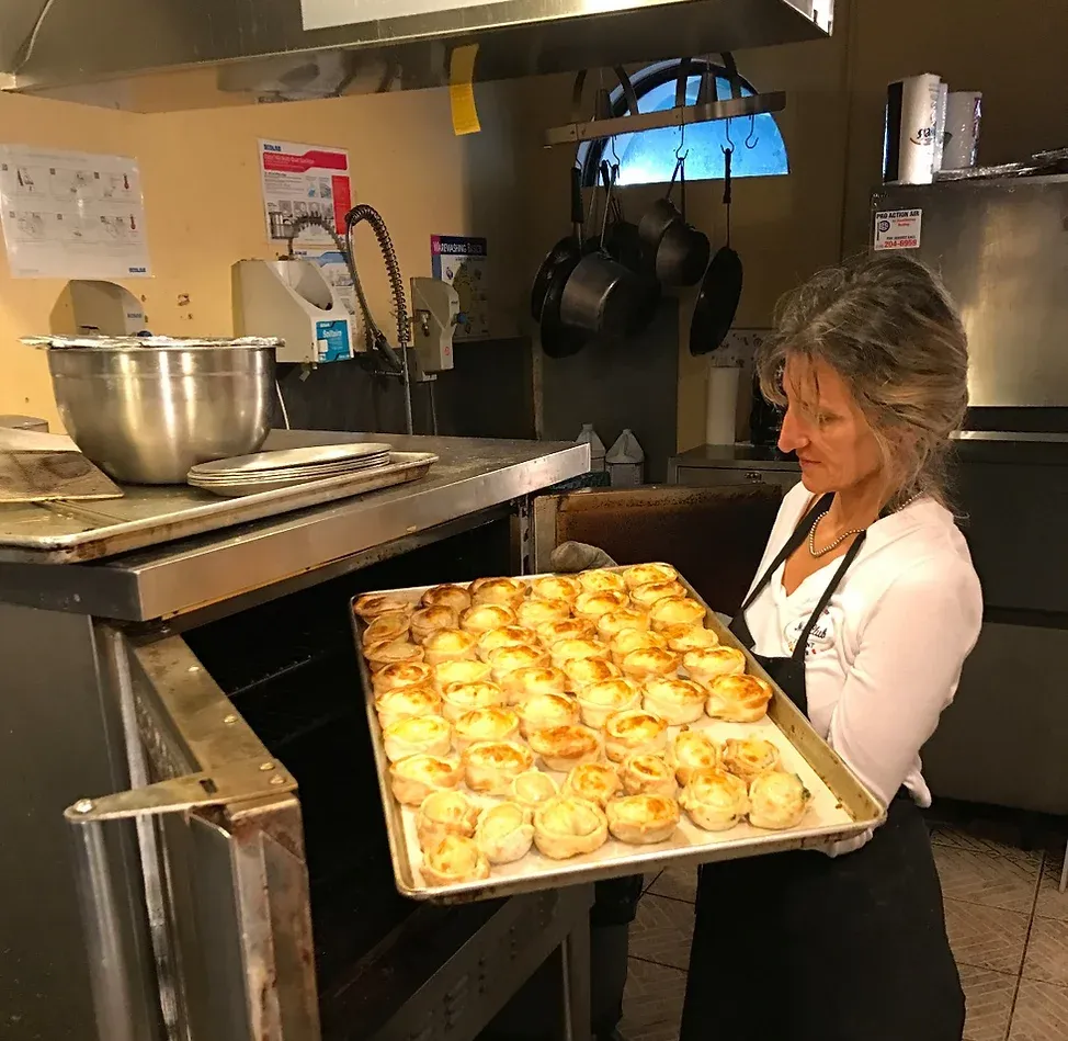 Woman removing tray of baked goods from an oven in a kitchen.