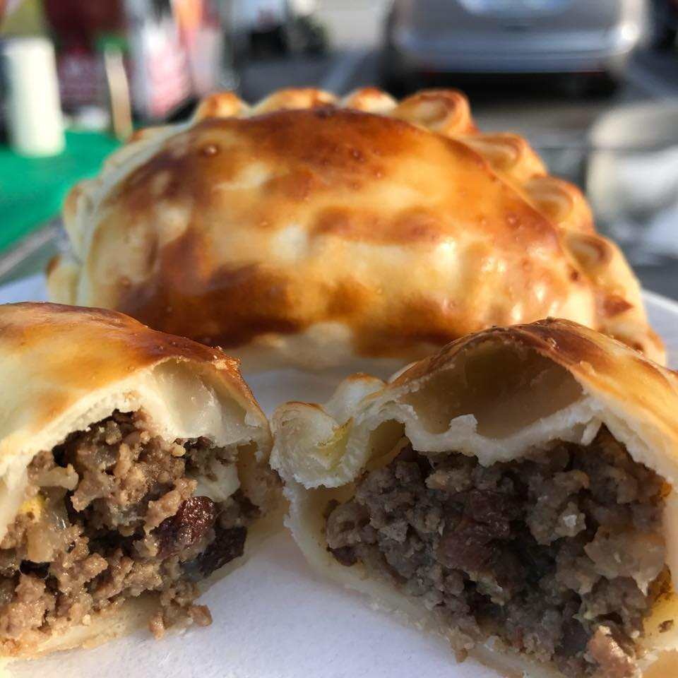 Close-up of an empanada cut open, showing a meat filling, and another whole empanada behind it.