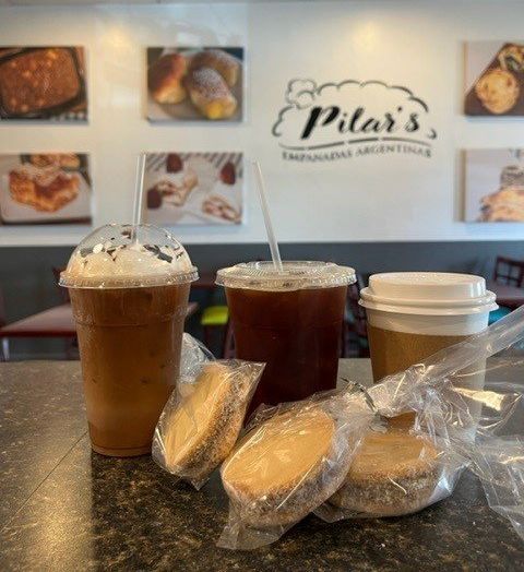 Iced coffee, alfajores, and a hot drink on a counter at Pilar's Empanadas Argentinas.