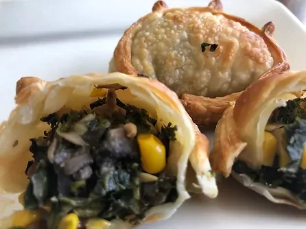 Close-up of three empanadas, two cut open to show filling of greens, corn, and mushroom.