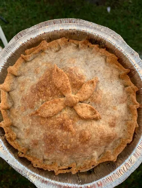 Baked apple pie in a foil tin, golden crust with a decorative cutout.