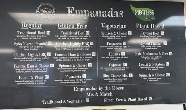 Menu board listing various empanada flavors: regular, gluten-free, vegetarian, and plant-based options.