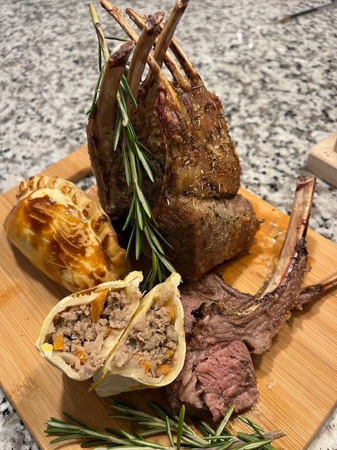 Rack of lamb with a pastry and sprigs of rosemary on a wooden board.