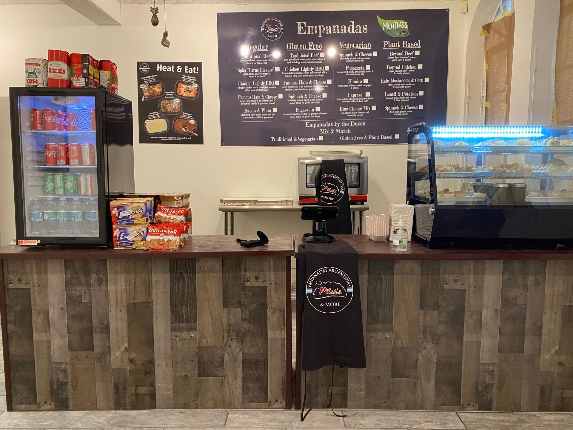 Counter in an eatery with menu, fridge, snacks, and baked goods display.