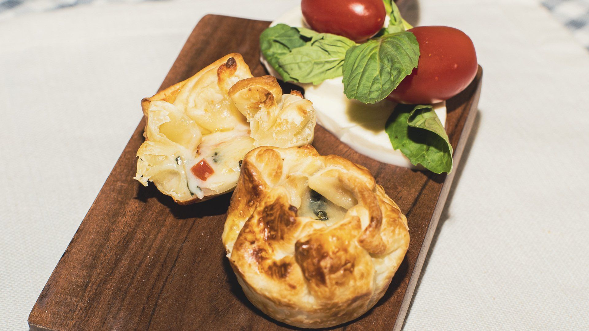 Appetizer platter: pastries and caprese salad on a wooden board.
