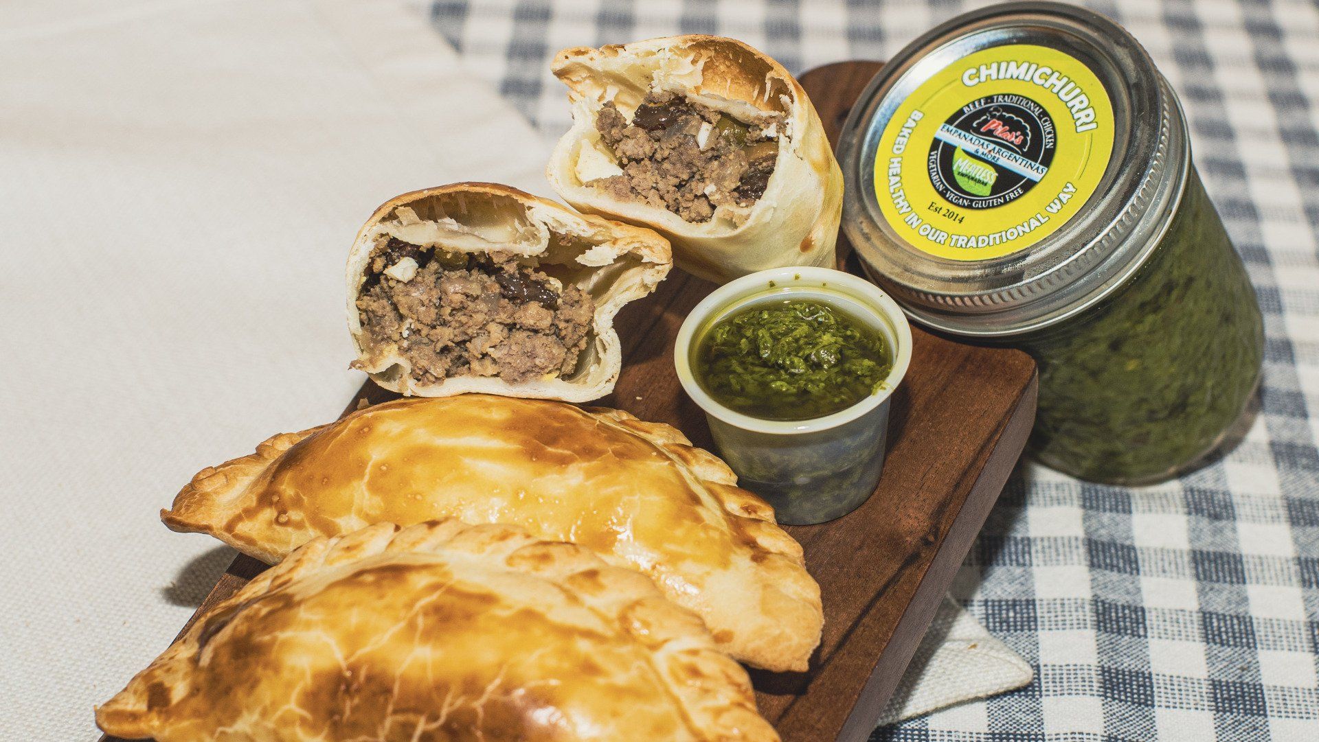 Savory pastries and jar of green sauce on wooden board.