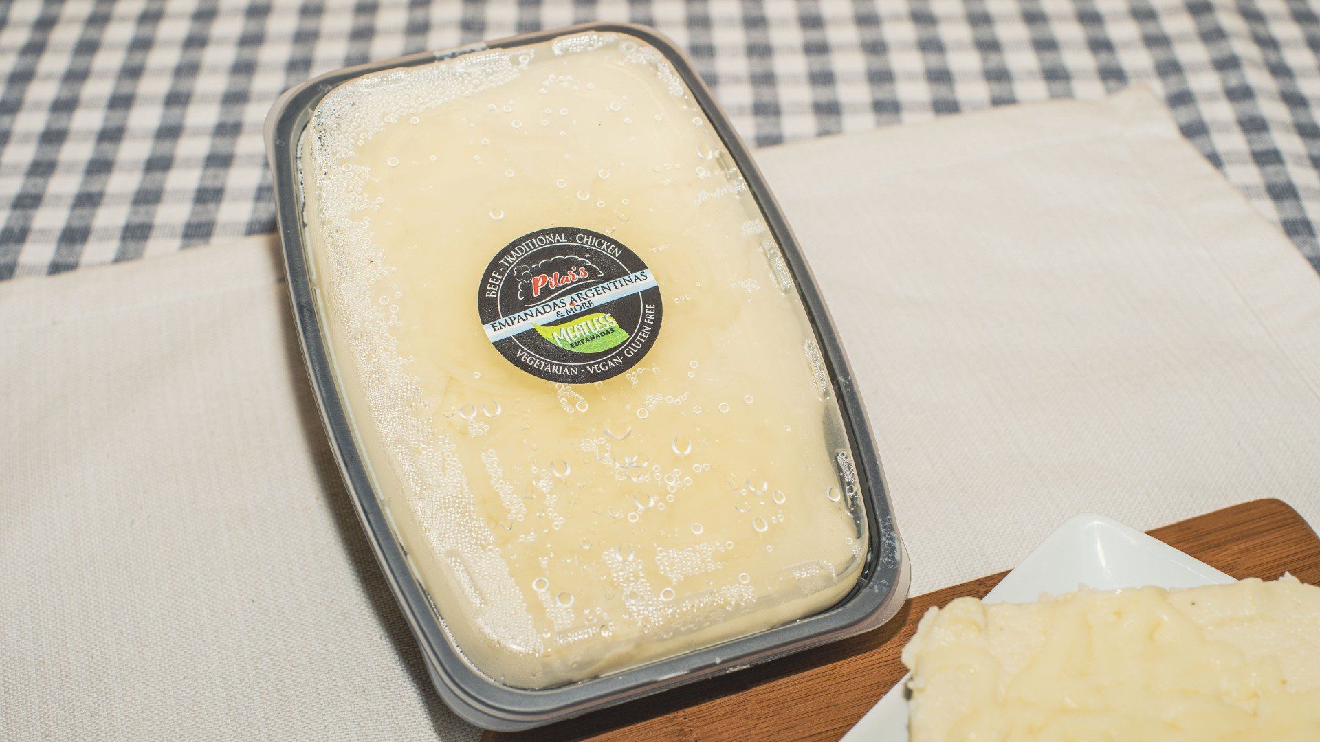 Butter in a plastic container with a label, set on a checkered tablecloth.