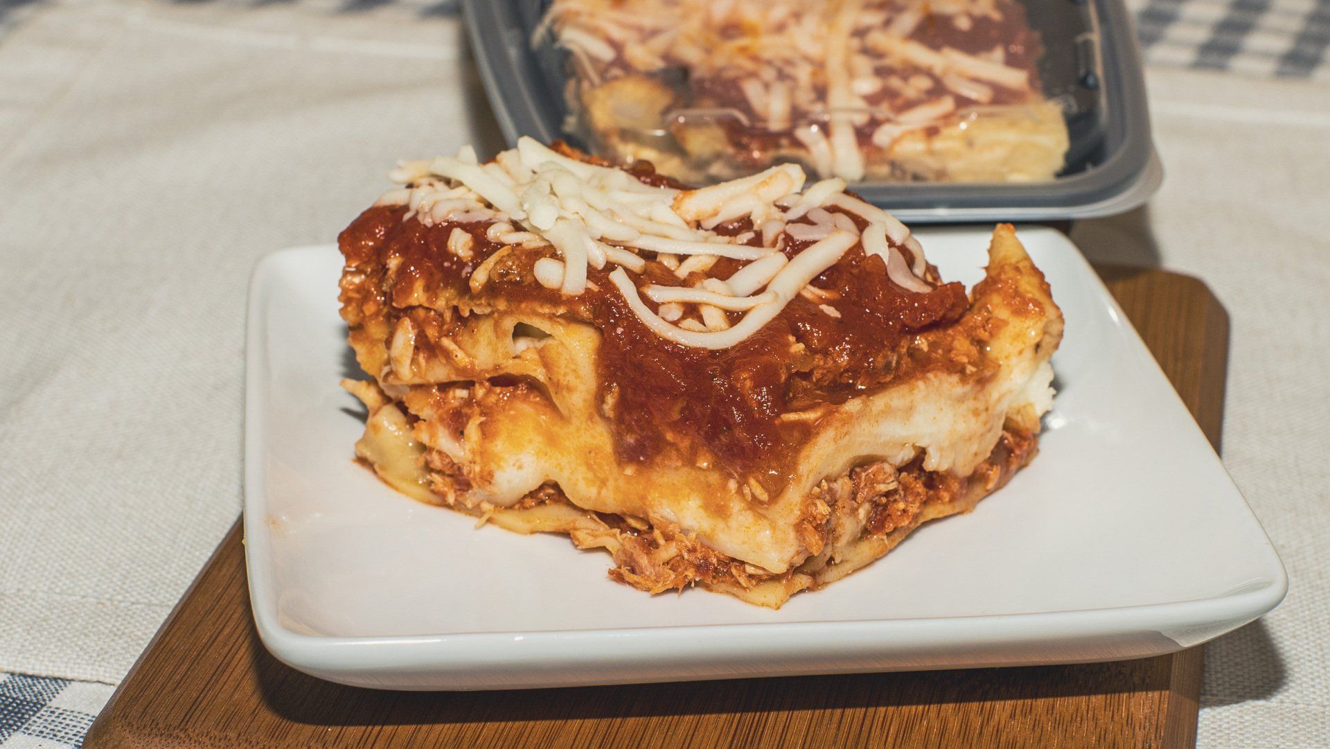 Lasagna slice on a white plate with a frozen lasagna tray in the background.