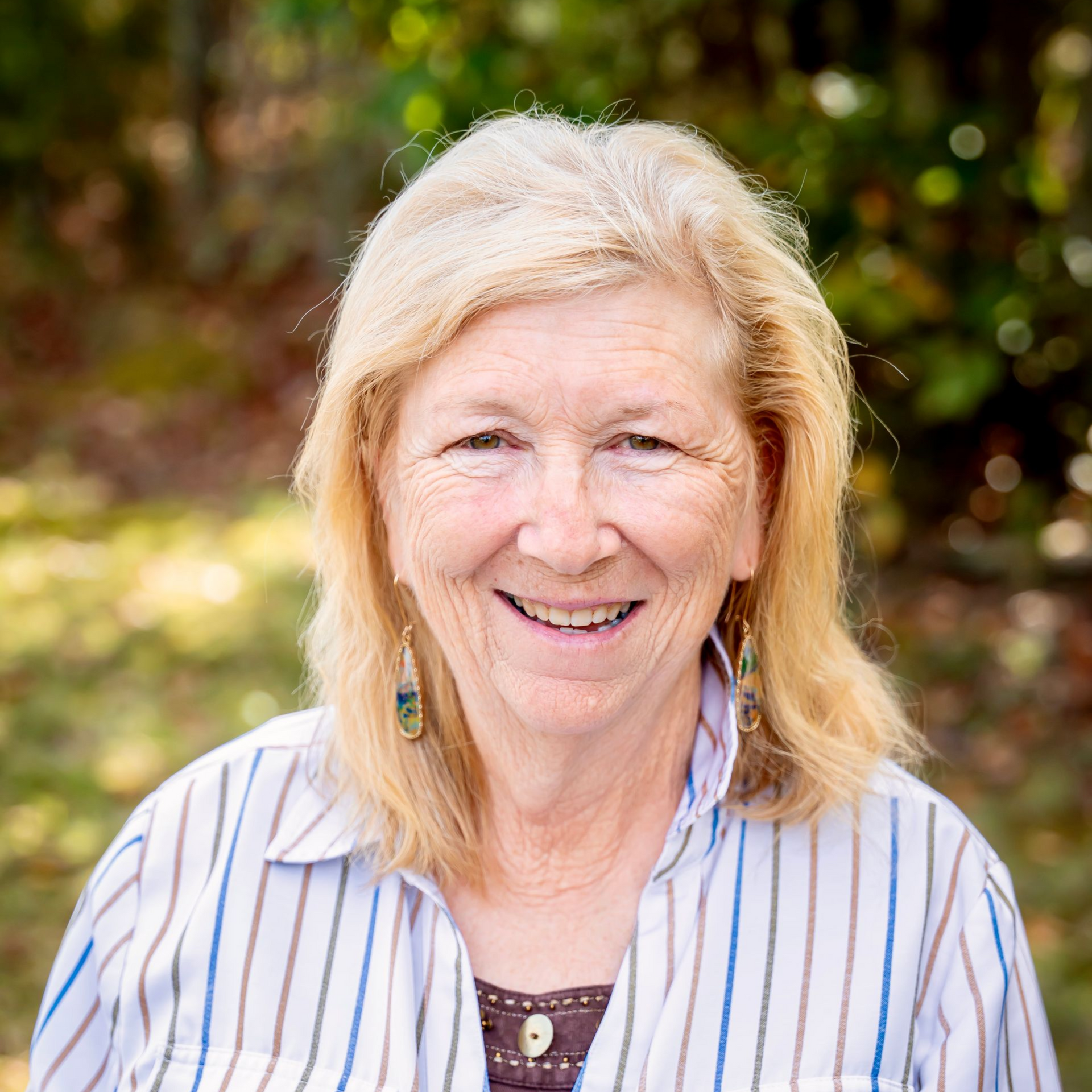 Woman with blonde hair wearing a striped shirt smiles outdoors.