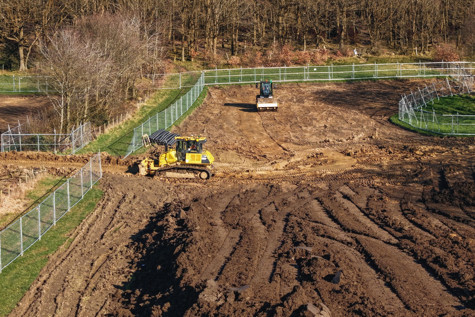 Bulldozers grading a muddy hillside construction site with fences and trees in the background