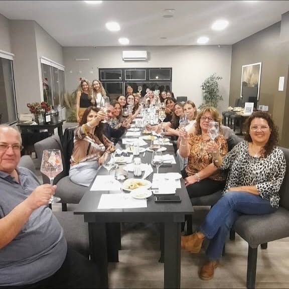 Un grupo numeroso cenando en una mesa larga en el interior, sonriendo y brindando durante una comida compartida.
