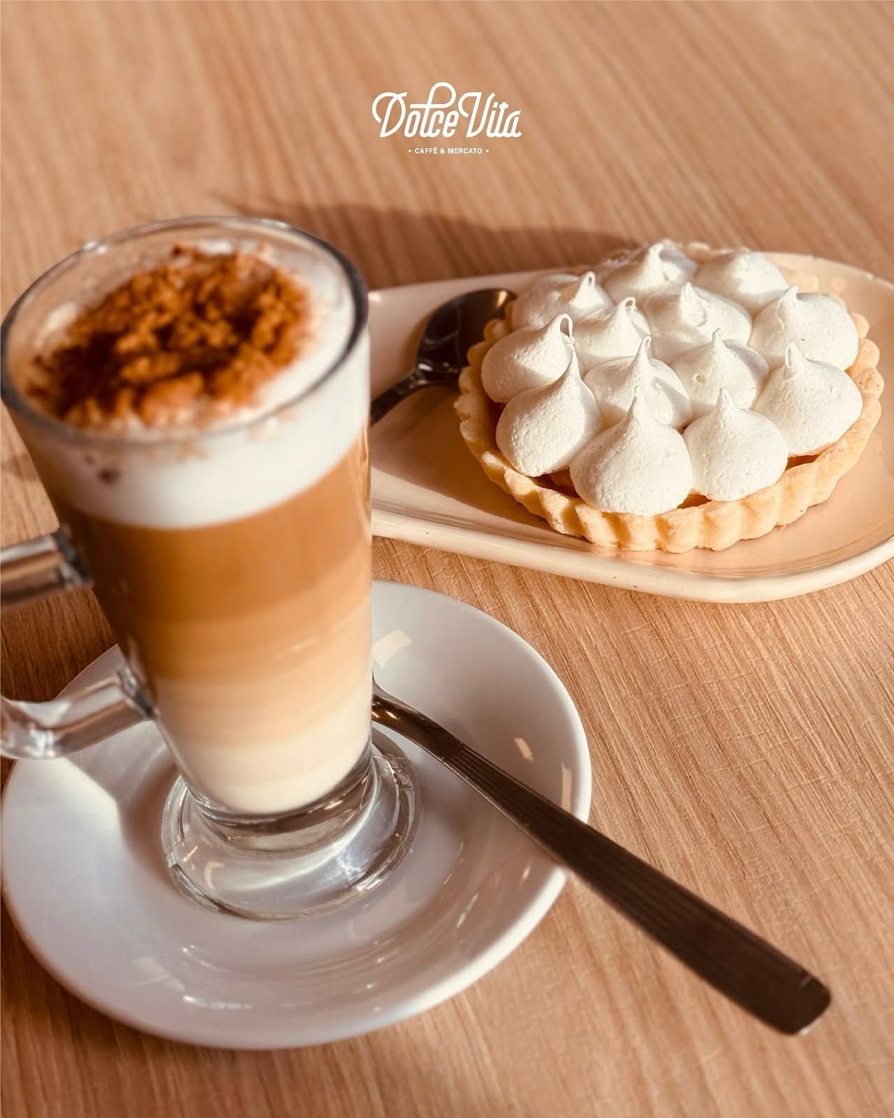 Un café con leche helado con capas de espuma junto a una tarta cubierta de crema sobre una mesa de madera.