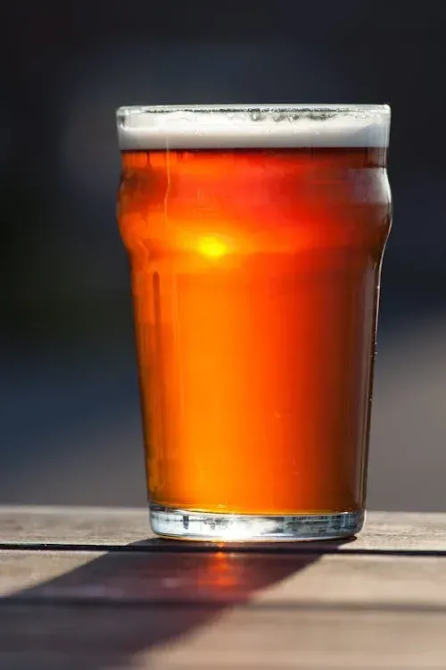 A glass of beer is sitting on a wooden table.