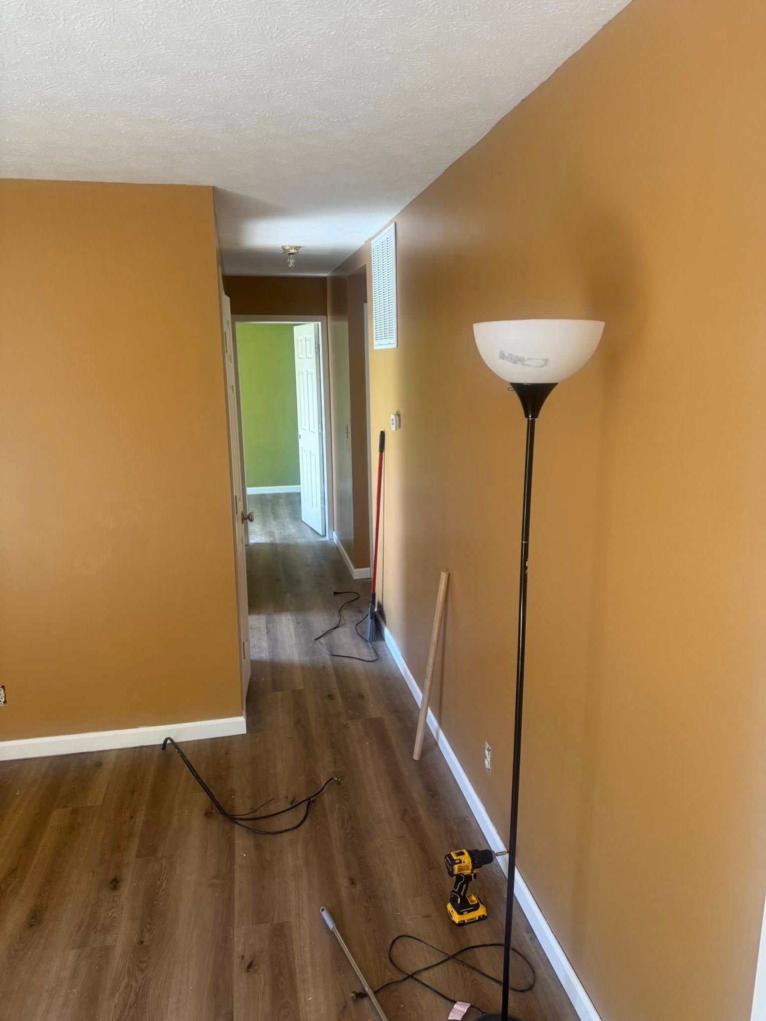 Empty hallway with tan walls, wood floor, floor lamp, and loose cords near a doorway.
