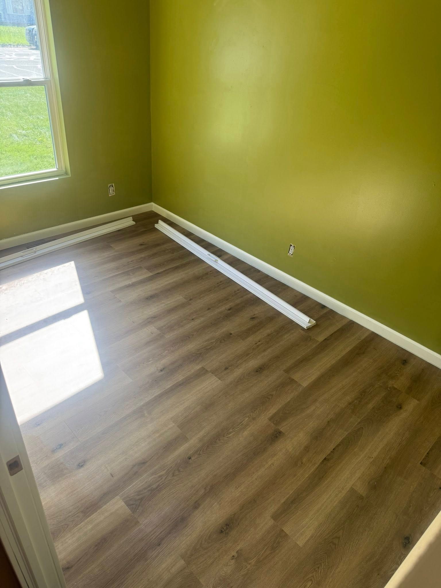 Empty room with lime-green walls, wood-look flooring, and a window letting in bright sunlight.