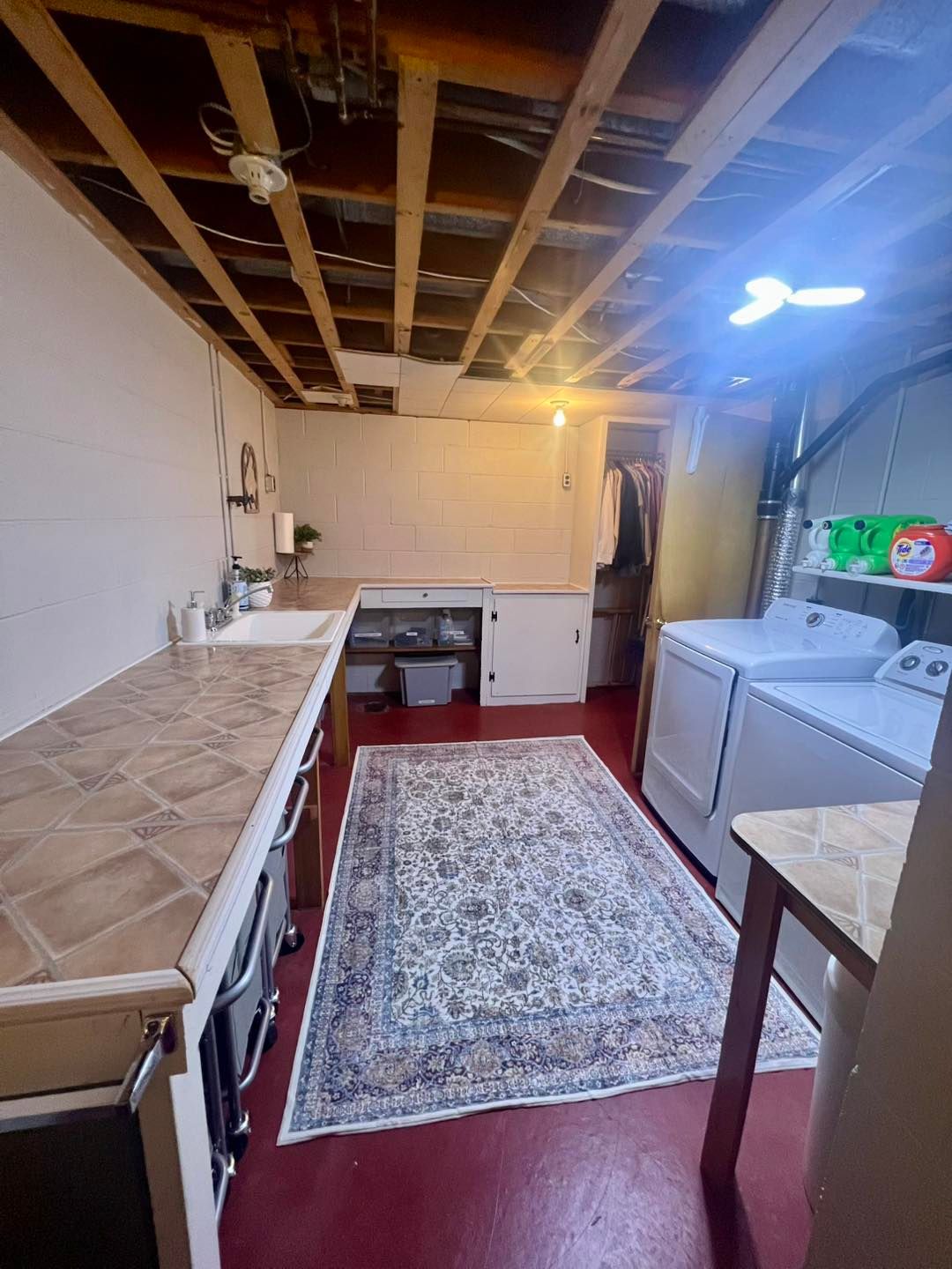 Small kitchen with exposed ceiling, white appliances, red floor, and a patterned rug.