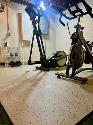 Home gym with two stationary exercise bikes on a carpeted floor in a room with mirrors and wall-mounted equipment