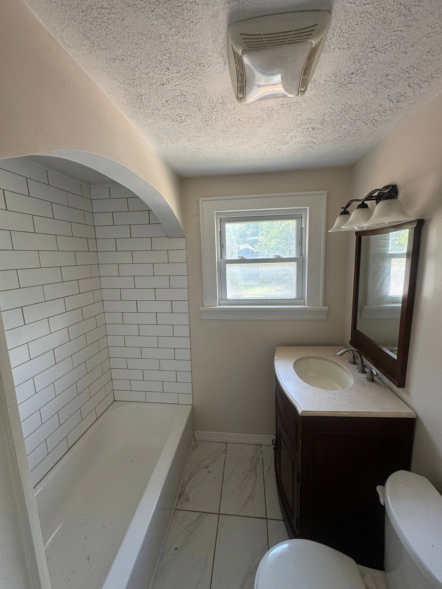 Small bathroom with white tile shower, vanity, window, and light-colored walls and ceiling.