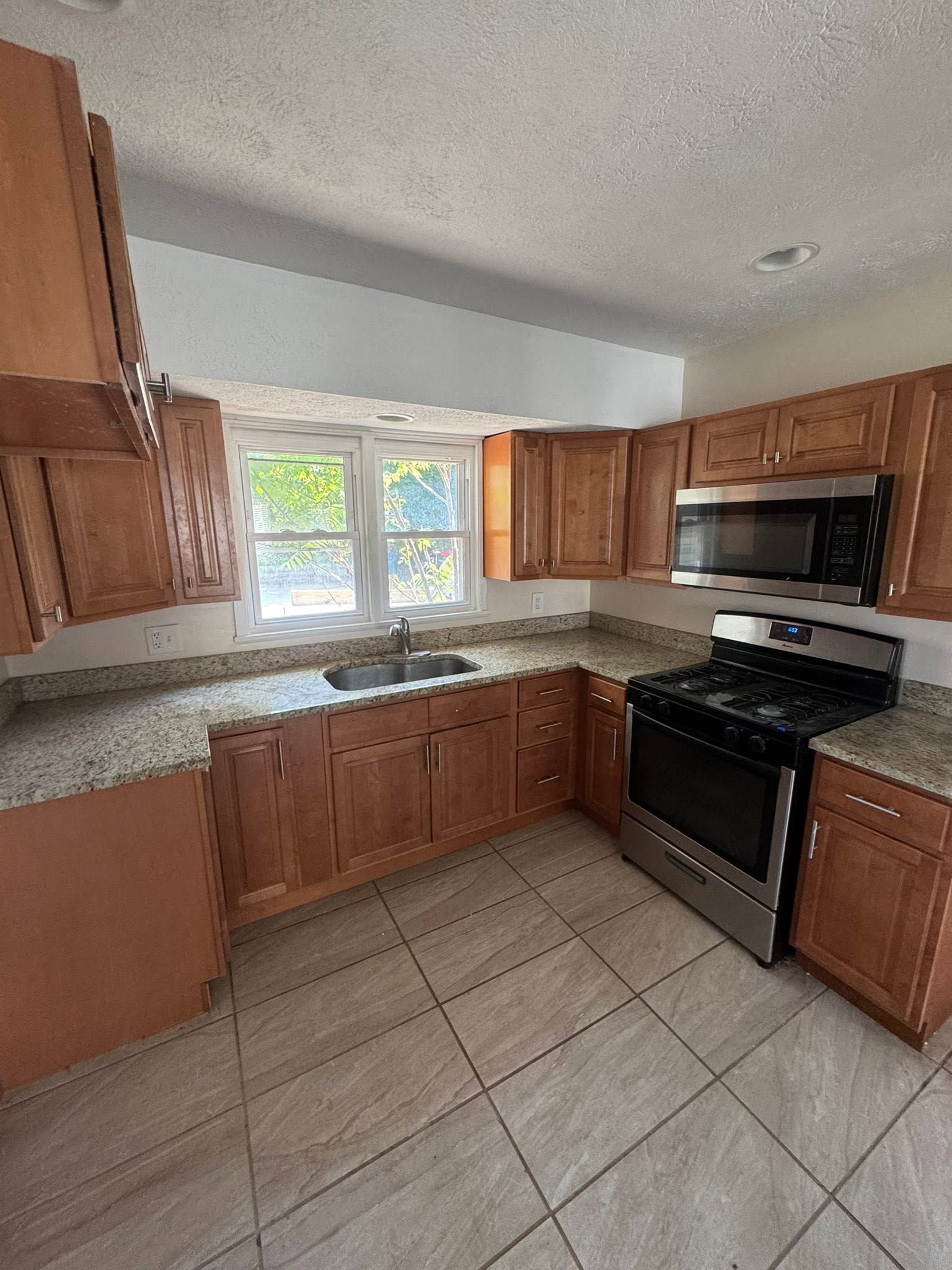Small kitchen with wood cabinets, granite counters, black appliances, and a window over the sink.