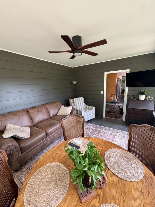 Living room with brown leather sofa, patterned chairs, round wooden table, green walls, and ceiling fan