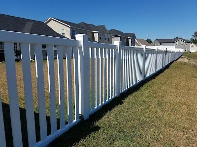 White picket fence bordering grassy lawn with suburban houses in background.