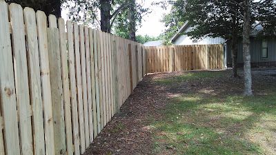 Wooden fence in a yard, next to grass and trees, with a house in the background.