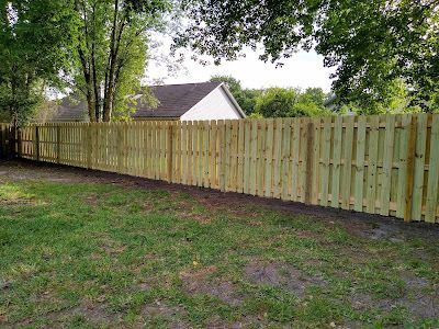 Wooden fence in a backyard with green grass and trees, a house in the background.