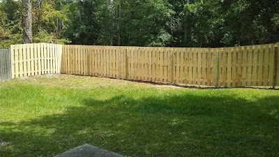 Wooden fence surrounding a grassy backyard with trees in the background.
