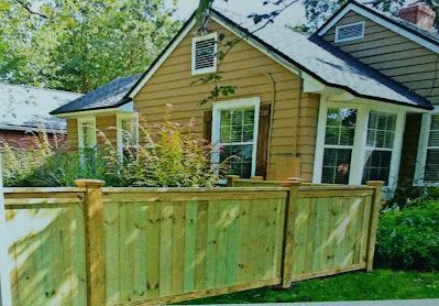 Wooden fence in front of a tan house with white trim and a red brick chimney.