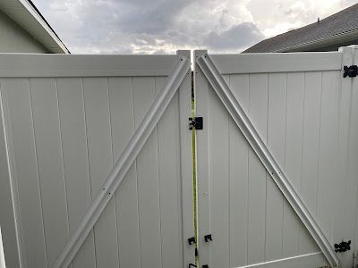 White double gate with diagonal bracing, black hardware, and cloudy sky.