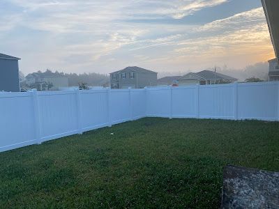 White fence encloses a green yard with houses in the background on an overcast day.