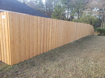 Wooden fence in a yard with brown grass and trees in the background.