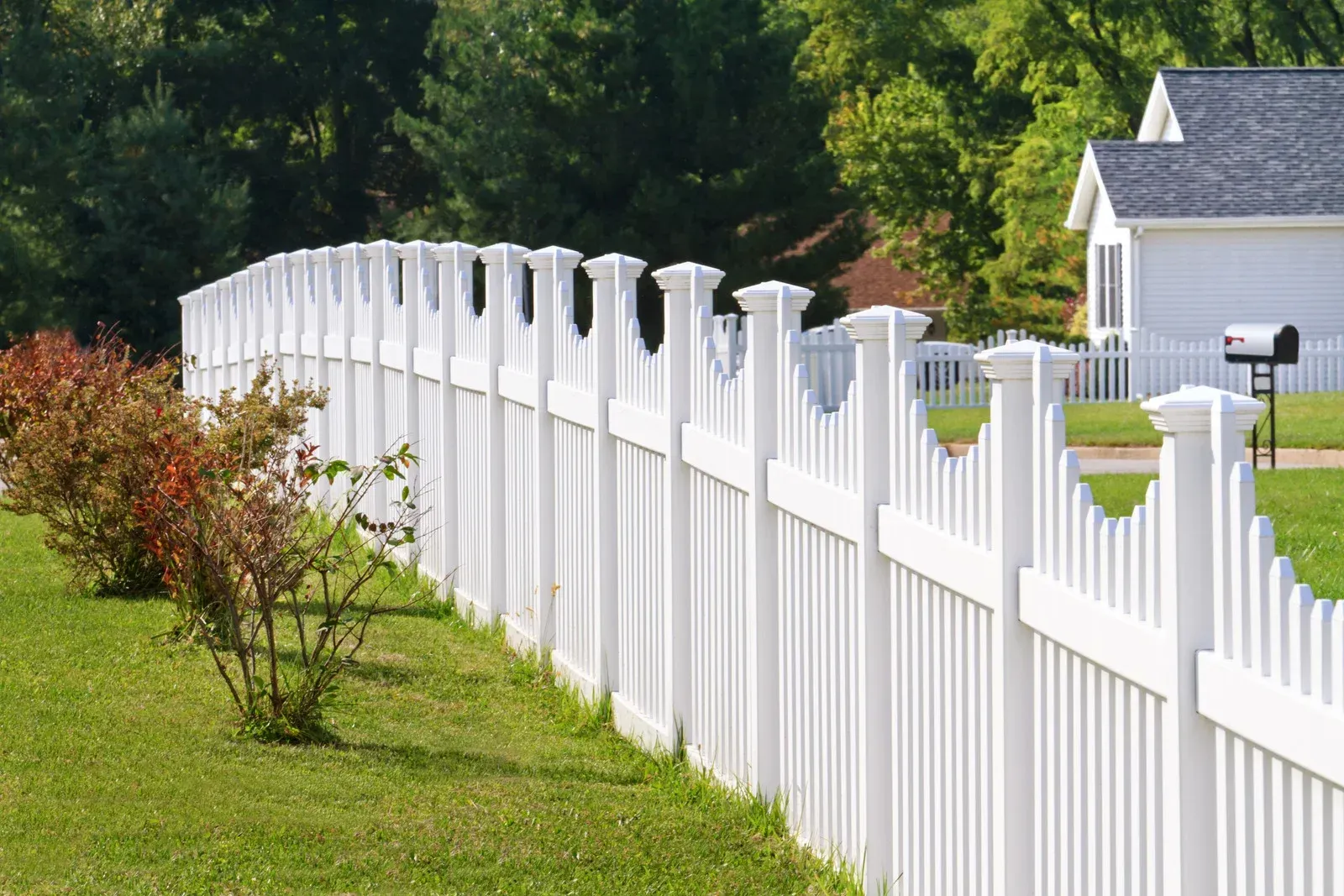White metal fence with open gate against a backdrop of trees and a blue sky.