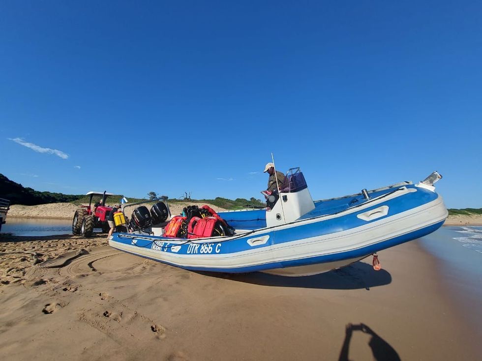Blue-and-white fishing boat beached on sand with people and gear under a clear blue sky