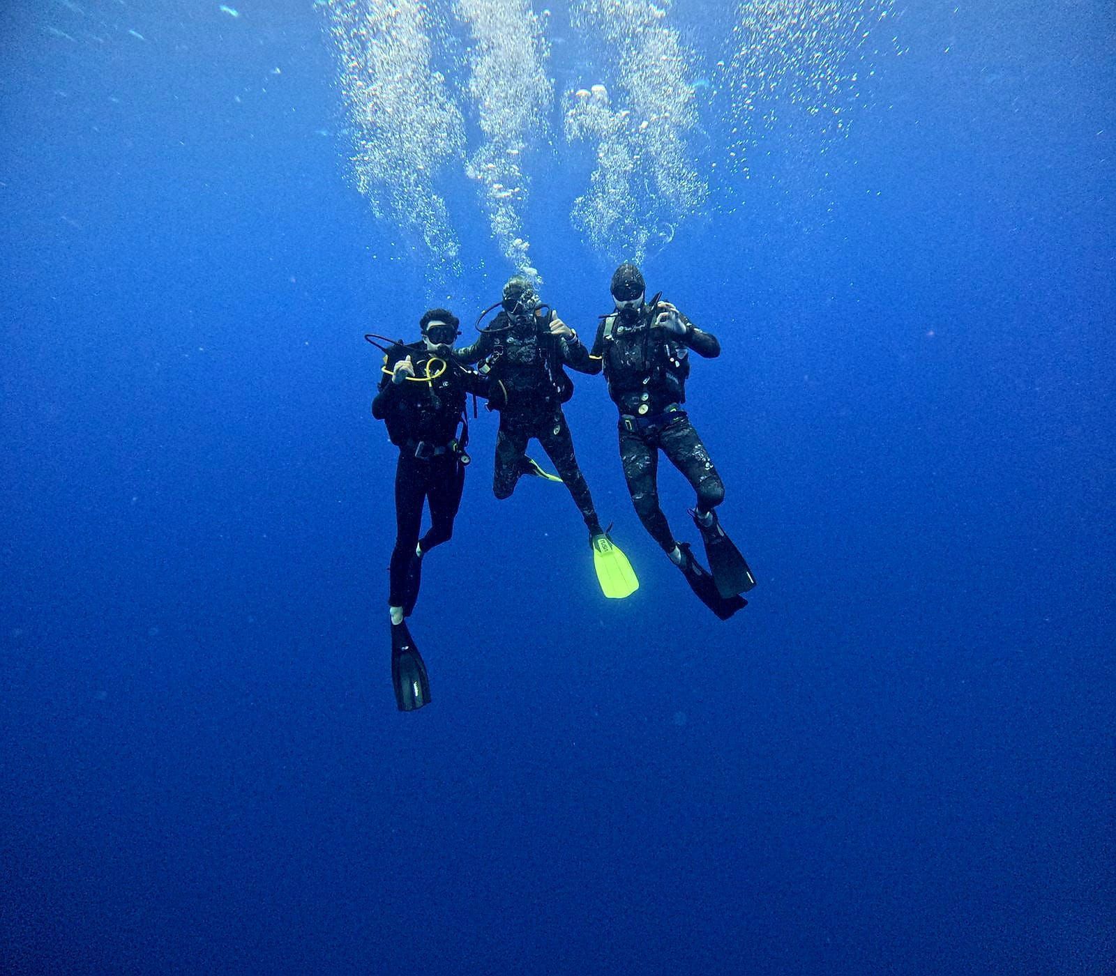 Three scuba divers swimming underwater in blue open water with bubbles rising above them