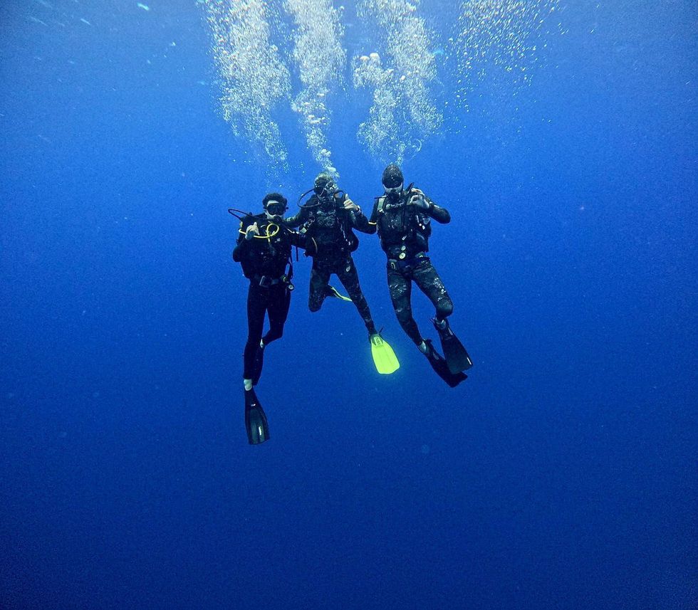 Three scuba divers swimming underwater in blue open water with bubbles rising above them
