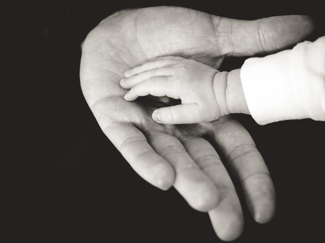A baby is holding a man 's hand in a black and white photo