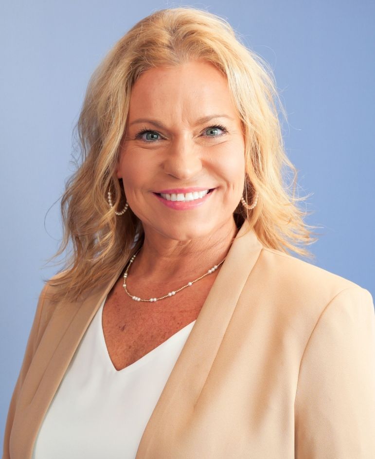 a woman wearing a tan jacket and a white shirt smiles for the camera
