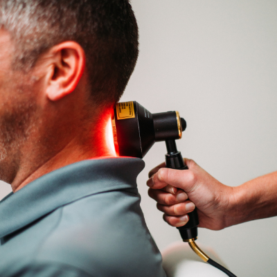 A person receiving red light therapy on their neck; held by a person.