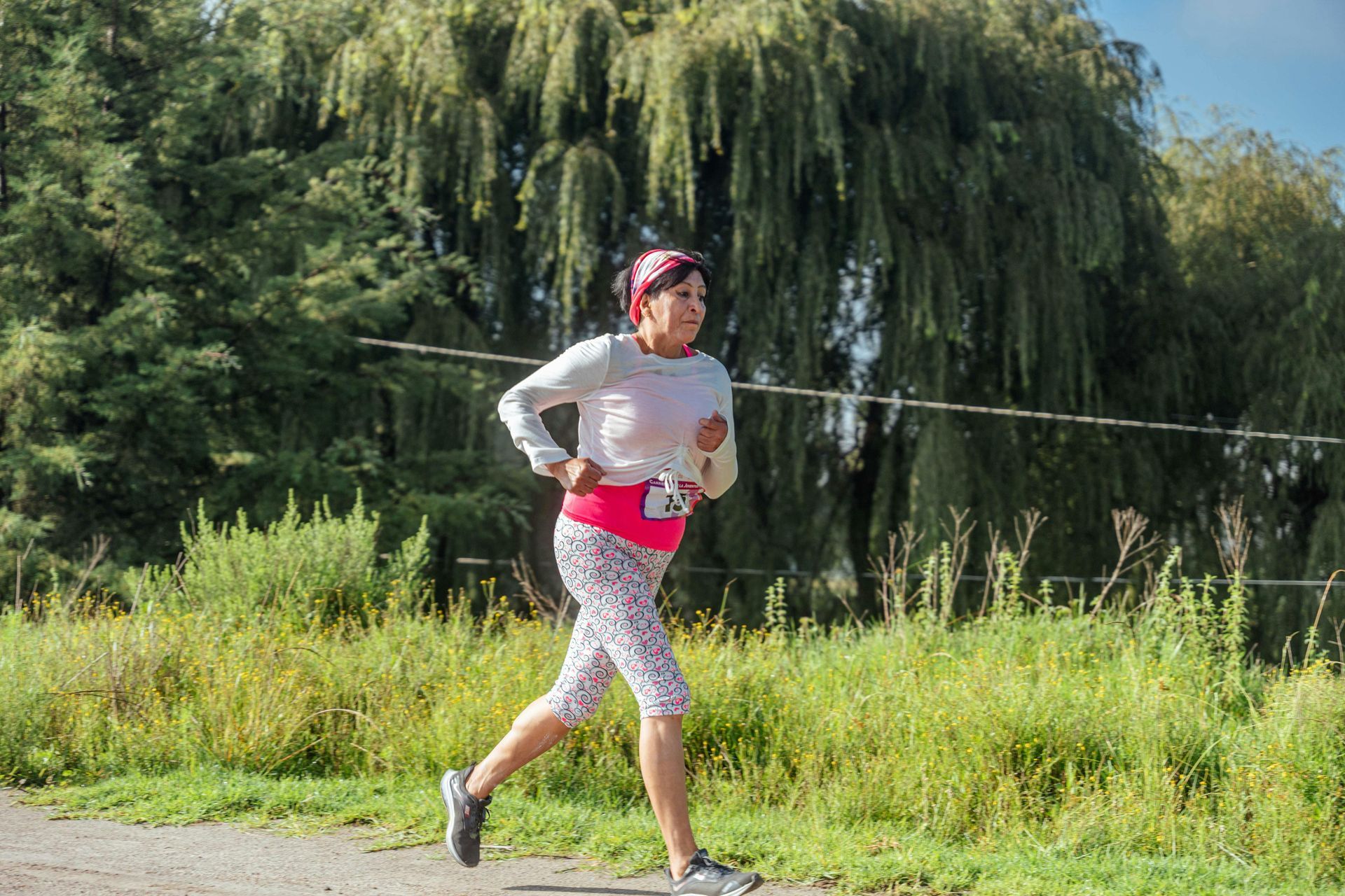 Runner in a red top and patterned leggings jogging on a trail with green trees in the background
