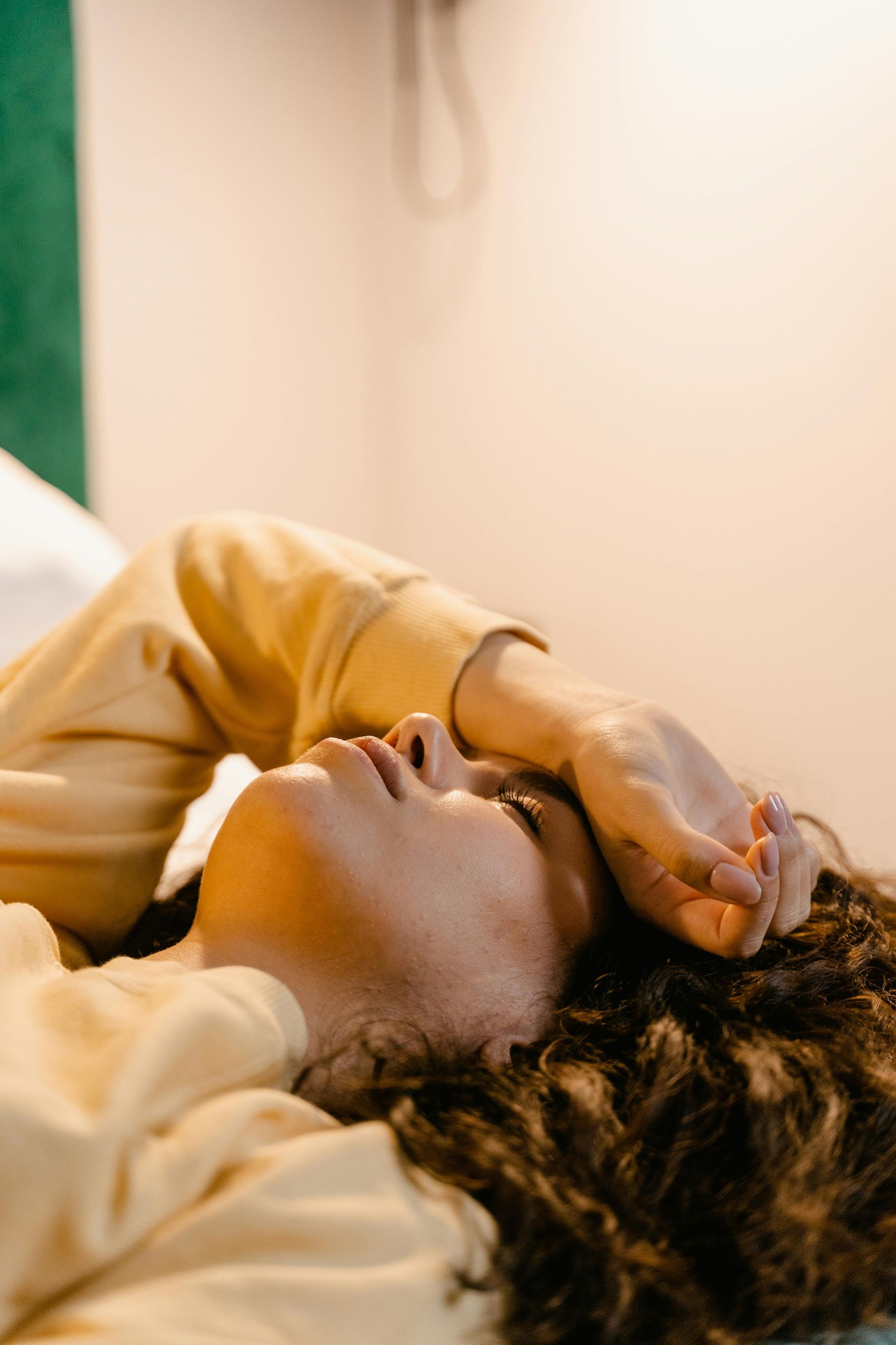 Person lying on a bed with hand over face, in warm light