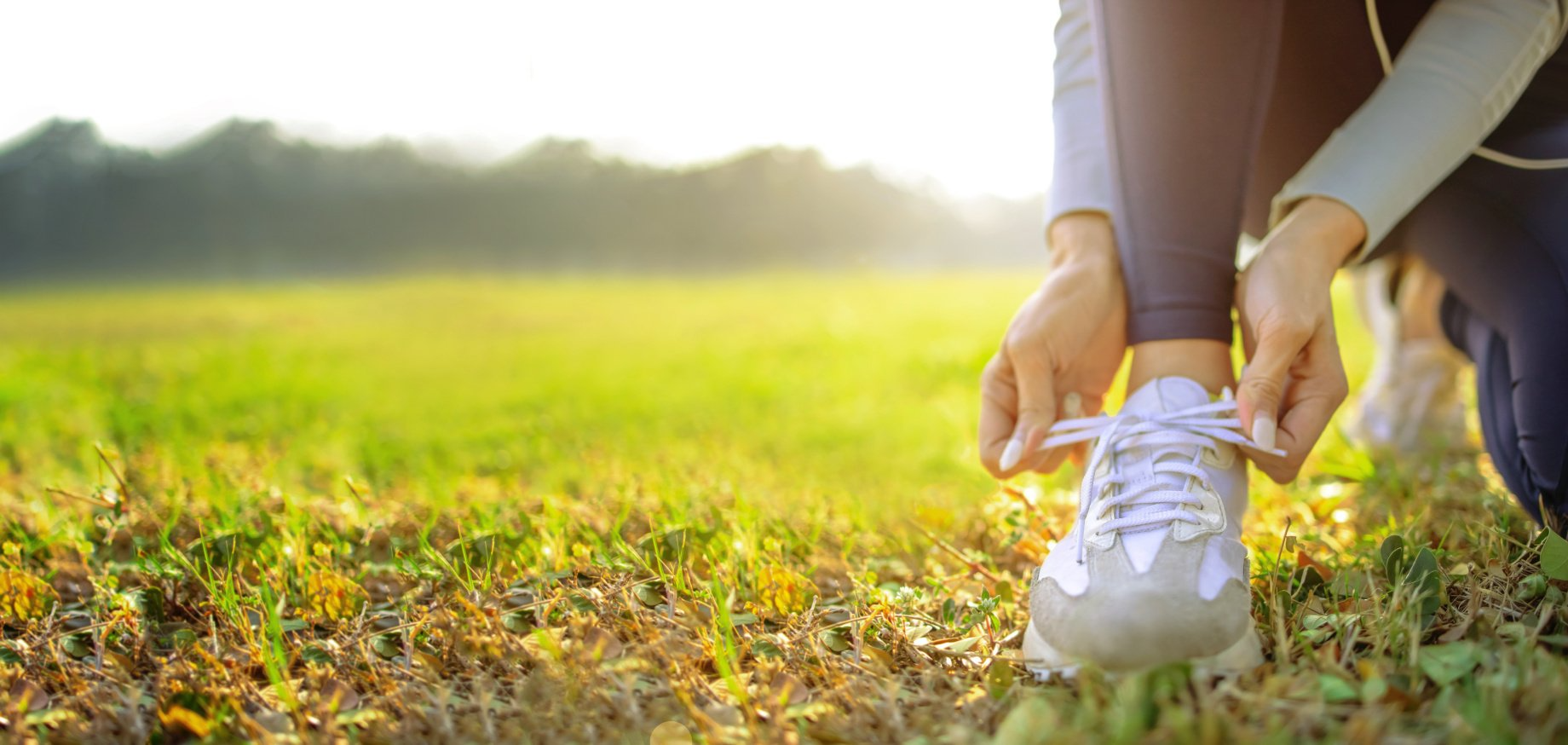 Woman tying her running shoe in a sunny field