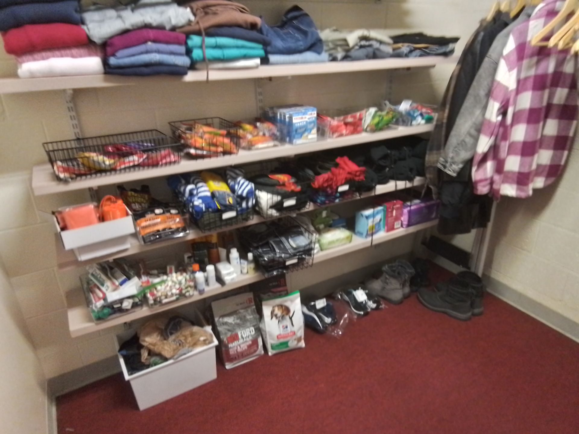 Shelves filled with clothing, toiletries, and snacks in a room with a red floor.