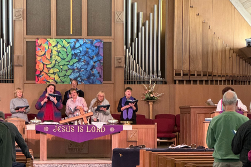Choir singing in a church with organ pipes, purple banner reading 